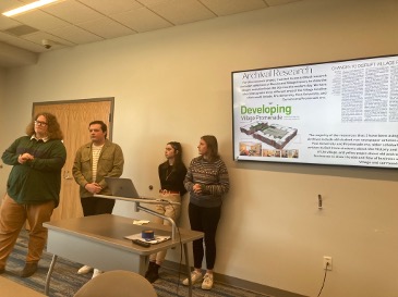Four students presenting a PowerPoint presentation of their research on The Village.
